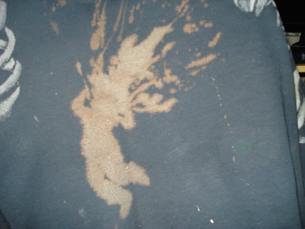 Close detail of a bleach-painted splatter and organic silhouette on dark fabric