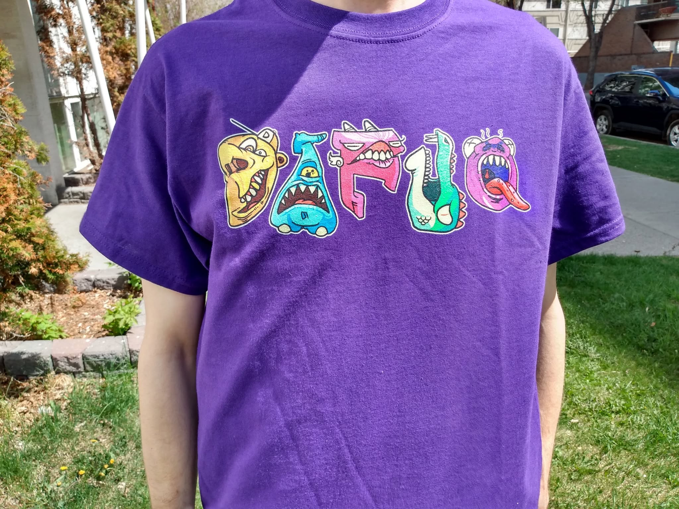 Close view of the printed DAFUQ monster-letter artwork on the purple shirt