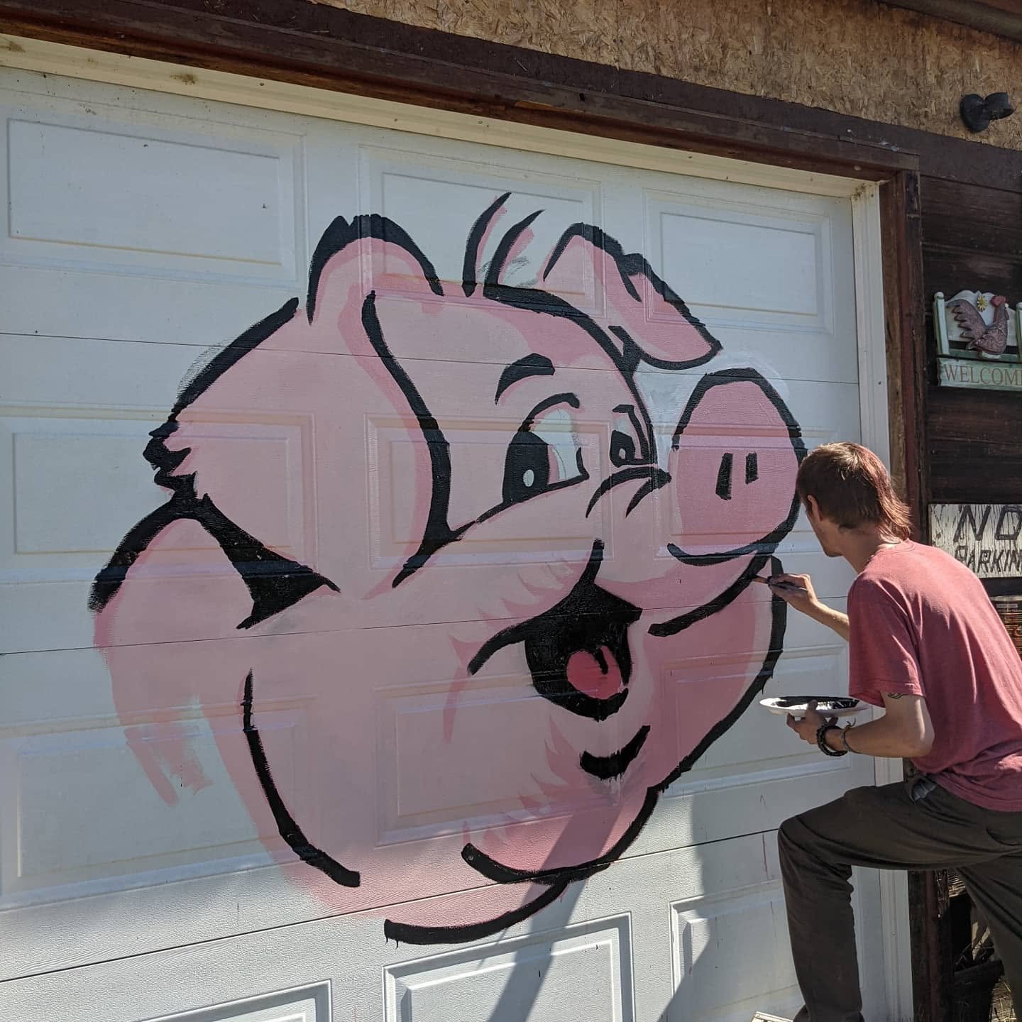 Derek Boe painting black linework over the pink block-in of the Hog Saloon mural